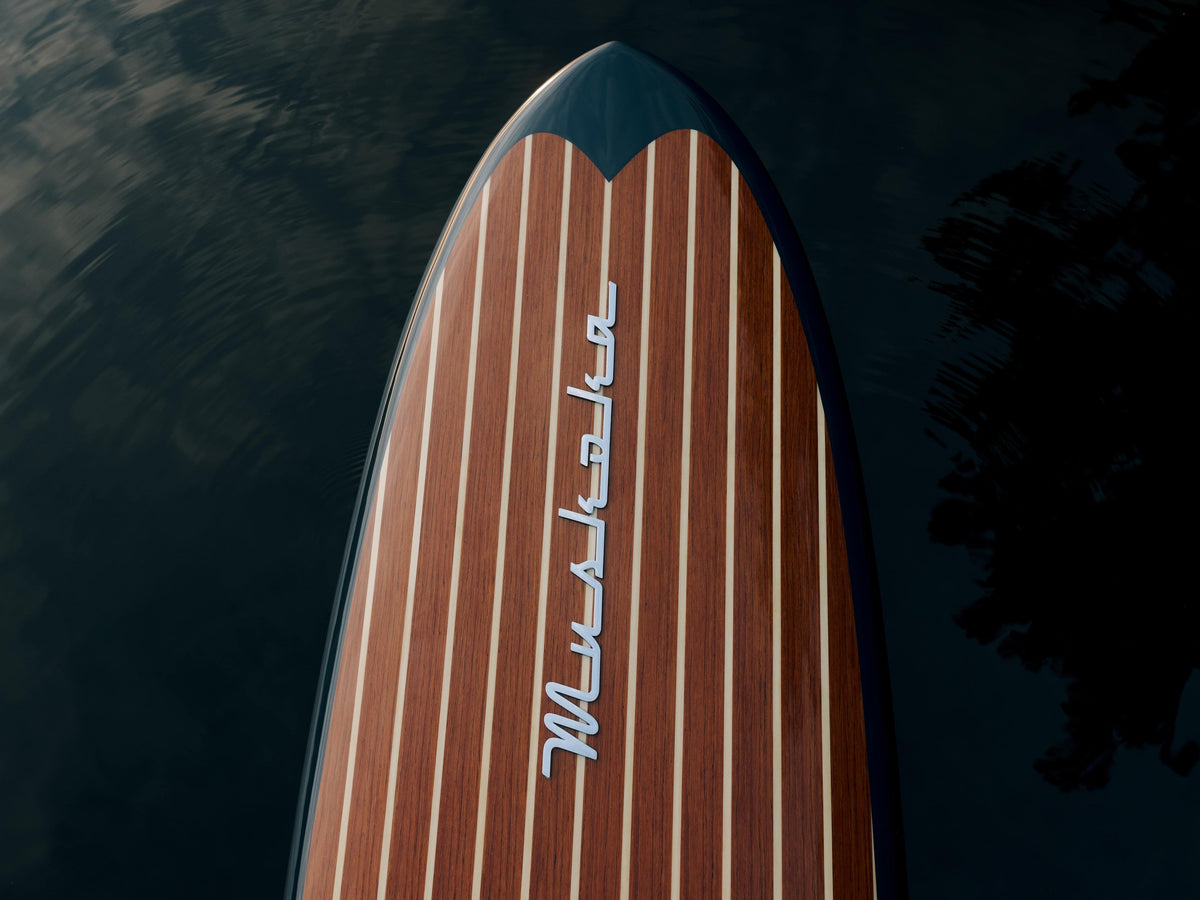 Close-up of the Beau Lake Muskoka paddleboard with rich wood veneer and white striping, floating on still dark water.