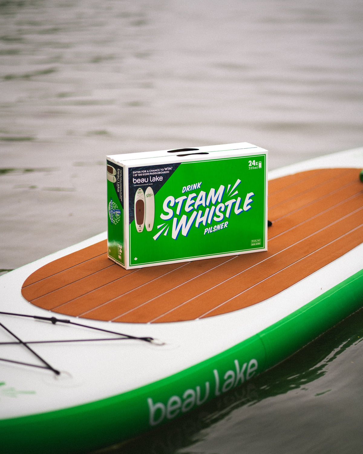 Steam Whistle beer case on Beau Lake paddleboard in calm water, promoting paddleboard giveaway collaboration.